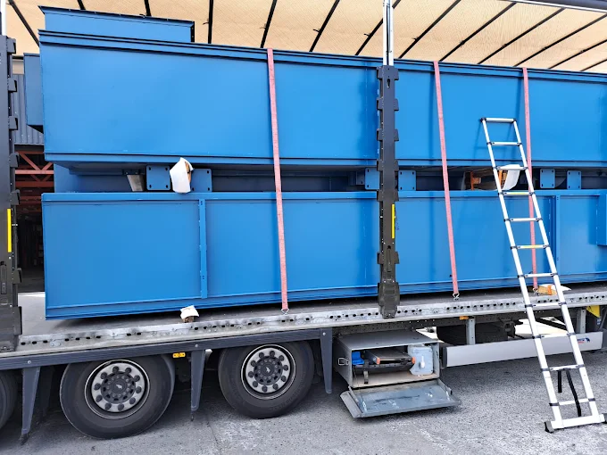 Załadunek dużych stalowych konstrukcji na naczepę ciężarówki, zabezpieczonych pasami transportowymi