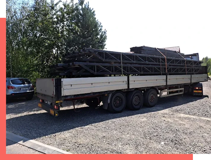 Ciężarówka z przyczepą załadowaną metalowymi konstrukcjami stalowymi, stojąca na parkingu obok samochodu osobowego