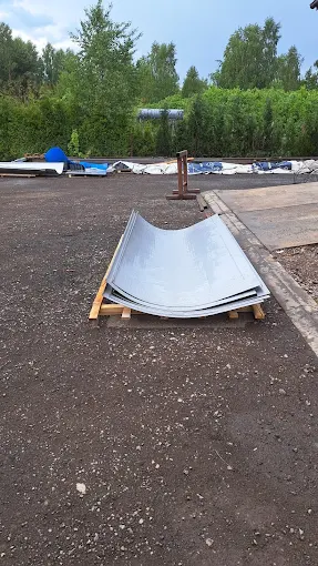 Zakrzywione blachy metalowe ułożone na drewnianej podstawie na placu z nawierzchnią asfaltową.